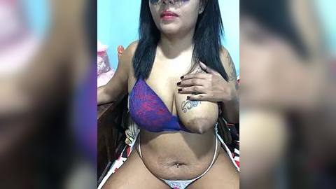 Media: Video of a Latina woman with long black hair, wearing a purple lace bra and white panties, sitting on a bed, holding her breast.