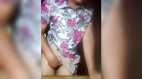 Media: Video of a woman in a floral-patterned shirt lifting her beige shorts, revealing her genitals. The image is blurry, making it difficult to discern details.