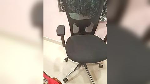 Media: Video of a black ergonomic office chair with a high backrest, positioned in a room with pink walls and white tiled floor. The chair is slightly blurry, with a red and black patterned garment draped over the back.