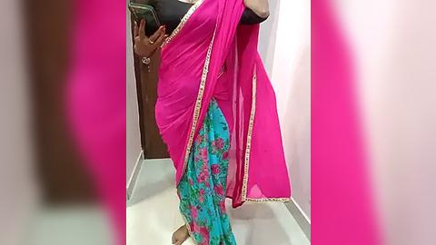 Media: A video shows a person wearing a vibrant pink and teal sari with intricate floral patterns, standing in a bright room with a wooden door and light-colored floor.