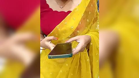 Media: Video of a woman in a vibrant yellow sari with intricate floral embroidery, wearing a red blouse and holding a smartphone, set against a blurred yellow background.