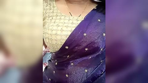 Media: Video of a woman's torso in a beige blouse with intricate embroidery and a purple sari with small white floral patterns, showcasing traditional Indian attire.