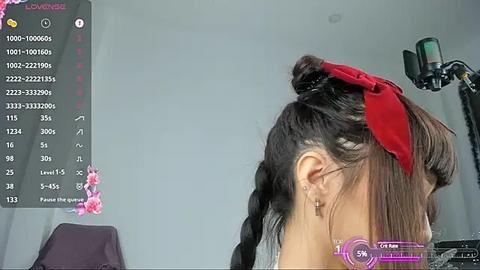 Media: A video of an Asian woman with braided hair adorned with a red ribbon, seen from the side, in a studio setting with a camera and lighting equipment.