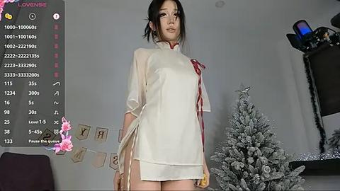 Media: A video of an Asian woman with black hair, wearing a sheer, white, high-collared dress with red accents, standing in a room with a Christmas tree and holiday decorations.