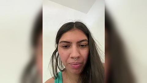 Media: Video of a young woman with long black hair, wearing a green tank top, and a septum ring, taken from a slightly blurred, frontal perspective.