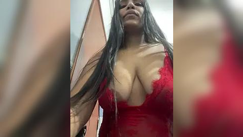 Media: Video of a curvaceous woman with long black hair, wearing a revealing red lace lingerie bra, standing in a dimly lit room with blurred background.