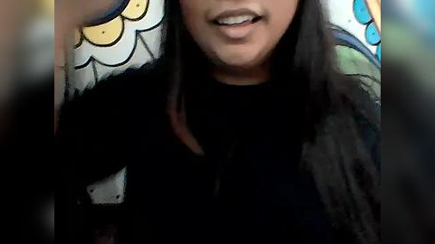 Media: Video of a woman with medium skin tone, wearing a black shirt, and a colorful, patterned scarf with a cartoonish design. Her long, straight dark hair falls over her shoulders.