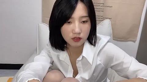 Media: Video of an Asian woman with short black hair and light skin, wearing a white shirt, sitting on a white chair in a clinical setting.