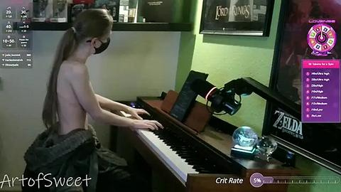 Media: Video of a topless, slender young woman with long blonde hair, playing a keyboard in a dimly lit room. The room has a TV screen displaying a game, a laptop, and a camera on the keyboard.