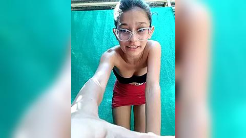 Media: Video of a young Asian woman with glasses, wearing a strapless red dress, bending forward, and holding a bandaged hand.