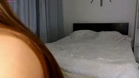 Media: Video of a bedroom with a fluffy white bedspread, a dark wooden headboard, and a partially visible person with long brown hair.