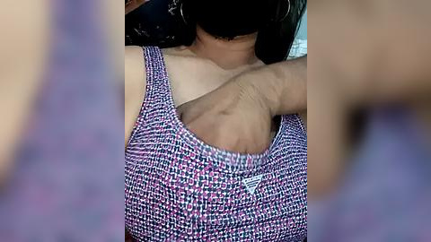 Media: Video of a woman with fair skin, wearing a patterned, sleeveless, purple top, scratching her armpit with her right hand. Background is blurred.