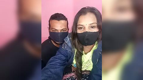 Media: A video of two South Asian individuals with short dark hair, wearing black face masks and denim jackets, against a pink backdrop.