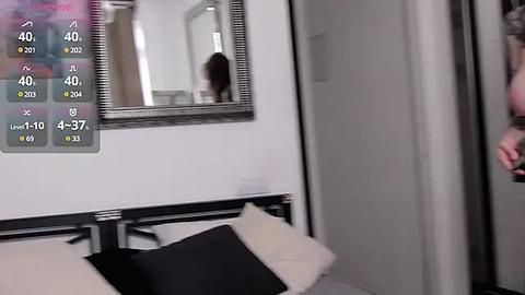 Media: Video of a modern bedroom with a large mirror reflecting a person's blurred silhouette, a bed with white and black pillows, and a digital overlay displaying health metrics.