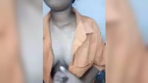 Media: A video of a person with light skin wearing an unbuttoned beige shirt, revealing a white bra, standing in a blurred, light blue background.