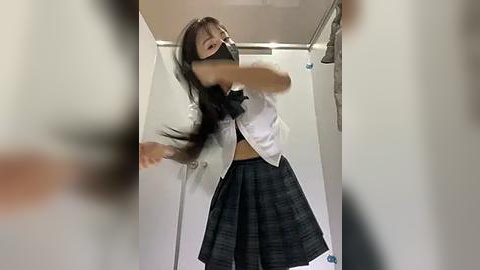 Media: Video of a young Asian woman in a schoolgirl outfit, black mask, and gray blazer, dancing energetically in a white-tiled hallway.