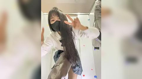 Media: Video of an Asian woman with long black hair, wearing a white jacket, gray skirt, and black face mask, dancing energetically in a cluttered bathroom with a shower curtain and hanging clothes.