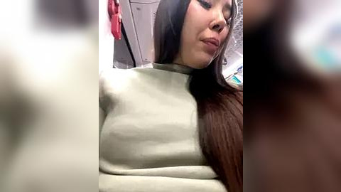 Media: A blurry video of a young woman with long brown hair and a light-colored, high-neck sweater, possibly taken on a plane, with a blurred background of passengers and overhead compartments.