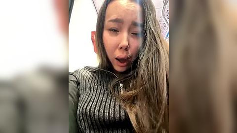 Media: A video of a young Asian woman with long, wet hair, wearing a grey knit top, looking upset and holding a phone.