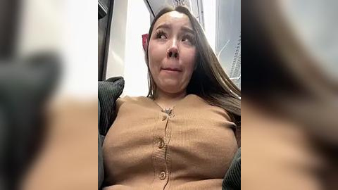 Media: A candid video of a woman with long brown hair, wearing a beige cardigan, seated on a train. Her expression is neutral. Background includes a blurred train interior.