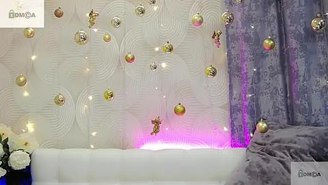 Media: Video of a modern, white, textured wall adorned with gold Christmas ornaments and fairy lights, set against a purple and gray, patterned backdrop.