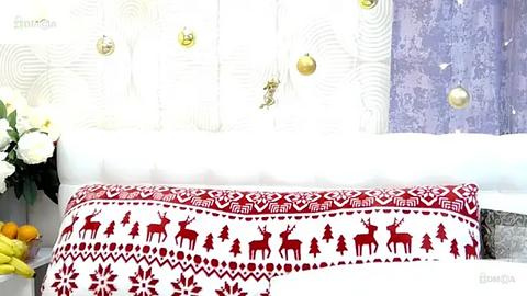 Media: Video of a festive bedroom with a white headboard featuring decorative gold ornaments and a red-and-white patterned cushion with reindeer, trees, and snowflakes.