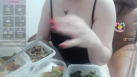 Media: A video of a fair-skinned woman in a black tank top, with a small tattoo on her chest, holding a black container. She's wearing red nail polish.