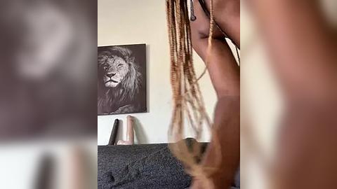 Media: Video of a person with dreadlocks, standing against a beige wall with a black-and-white lion print and a beige vase.