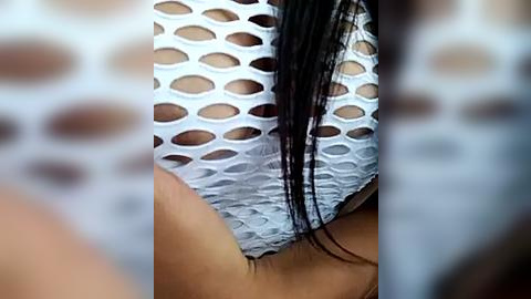 Media: Video of a woman with wet, black hair, wearing a white, mesh, cut-out bodysuit, revealing her toned, tanned midriff. Background features blurred, light-colored textures.