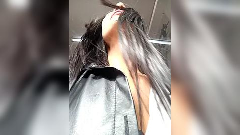 Media: A blurry video of a person with long, straight, dark hair wearing a black cape, standing in a salon with soft, diffused lighting. The image is slightly out of focus, emphasizing the subject's hair.