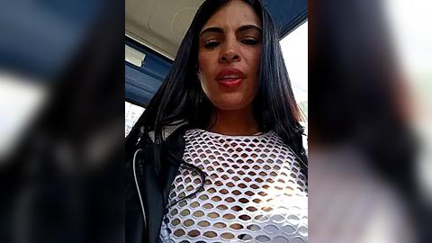 Media: A close-up video of a woman with long black hair, wearing a white fishnet top and black jacket, seen from a low angle, with blurred figures in the background.