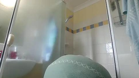 Media: A video of a steamy bathroom with a shower curtain, white tiles, a yellow and blue stripe, a teal towel, and a red bottle on a sink.