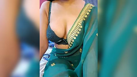 Media: Video of a South Asian woman in a green sari, revealing her cleavage in a black lace bra, with blurred background.