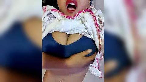 Media: Video of a woman lifting her white lace shirt to reveal a blue bra, showing cleavage and a glimpse of her bare chest, with her mouth open in an expression of surprise or pleasure.