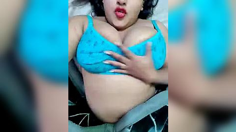 Media: Video of a plus-sized woman with dark skin, wearing a turquoise bra, lying on a car seat, with hands cupping her large breasts.