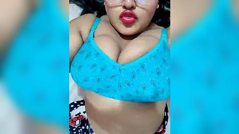 Media: A video of a plus-sized woman with fair skin and long black hair, wearing a turquoise bra with floral patterns, and a colorful skirt. She is pouting, with a playful, seductive expression.