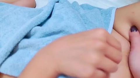 Media: Video of a close-up of a light-skinned person's hand grasping a blue towel, with part of a pink breast visible in the background.