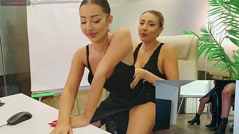 Media: Video of two women in black dresses, one lifting skirt, sitting at a white table in a modern office.