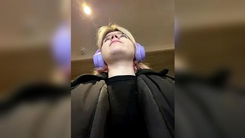 Media: Video of a person wearing large purple headphones, lying back in a black cape, with a blurred background.