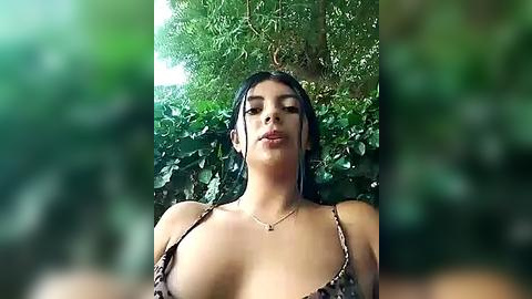 Media: A video of a young woman with olive skin and dark hair, wearing a leopard print bikini top, standing against lush green foliage. Her expression is serene, with closed eyes and parted lips.