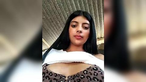 Media: Video of a young Latina woman with long black hair, light skin, and a medium build, wearing a white tank top and leopard-print bra, against a textured concrete wall background.