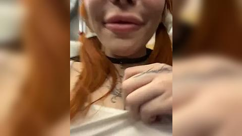 Media: Video of a close-up of a woman with fair skin and long, red hair, wearing a black choker. She has tattoos on her fingers and lips.