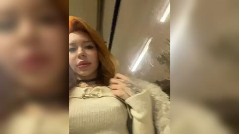 Media: A blurry video of a young woman with red hair, wearing a beige sweater and choker, standing in a dimly lit, beige-colored room with a door and window.