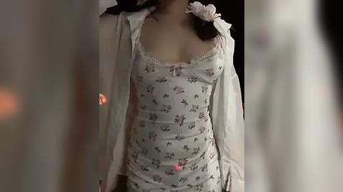 Media: Video of an Asian woman in a white floral camisole with lace trim, open cardigan, and a pink rose hairpin, standing indoors with blurred background.