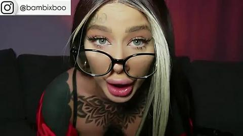 Media: Video of a fair-skinned woman with blonde hair and glasses, wearing a red top, showcasing extensive tattoo art on her neck.