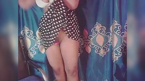 Media: A video captures a woman lifting her black-and-white polka-dotted dress, revealing her pink thong and toned legs, standing against a teal curtain with white floral patterns.