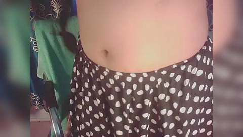 Media: Video of a person wearing black pants with white polka dots, revealing a flat stomach and navel. Background includes green and blue clothing.