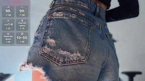 Media: A close-up video of a woman's lower back and buttocks in worn, light blue jeans with rips and frayed edges. Background shows a gray wall and digital interface with health metrics.