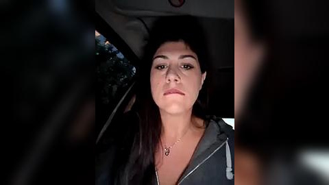 Media: Video of a young woman with long dark hair, wearing a black hoodie, sitting in the backseat of a car at night.