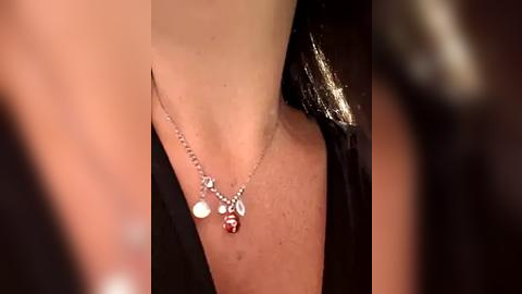 Media: Video of a close-up of a woman's neck adorned with a silver necklace featuring a red pendant and small pearls, set against a blurred background.